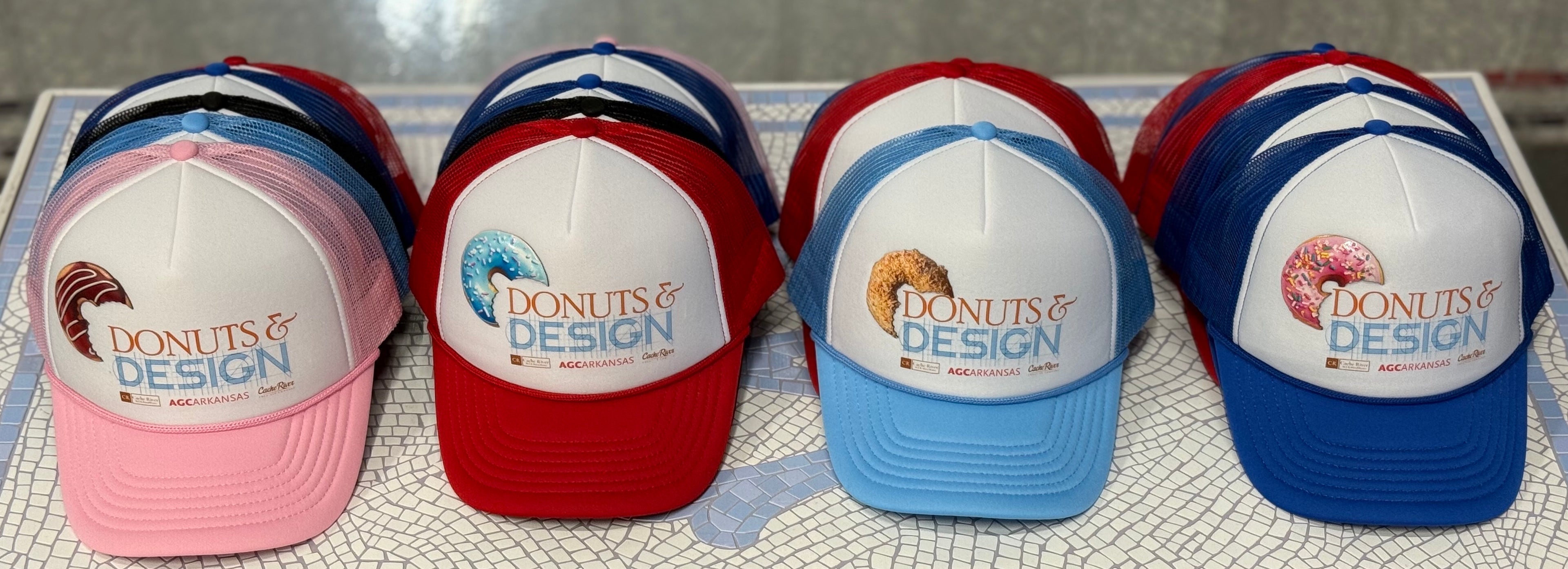 Four baseball caps with 'Donuts & Design' logo on a textured surface