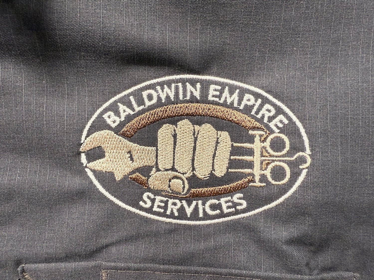 Embroidered logo on a dark fabric background with 'Baldwin Empire Services' text.